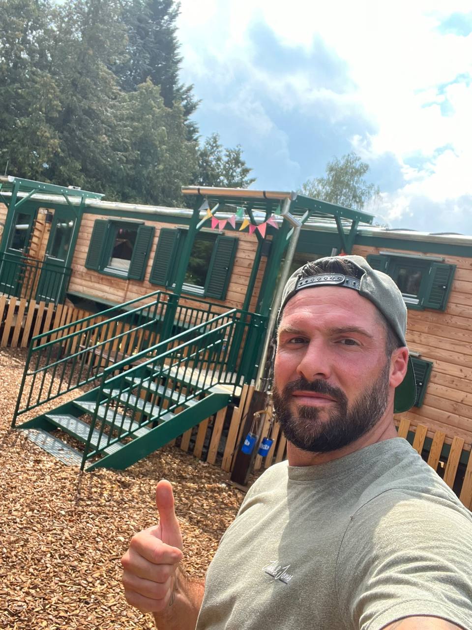 Jochen macht ein Selfie mit Daumen hoch vor dem Bauwagen eines Waldkindergartens